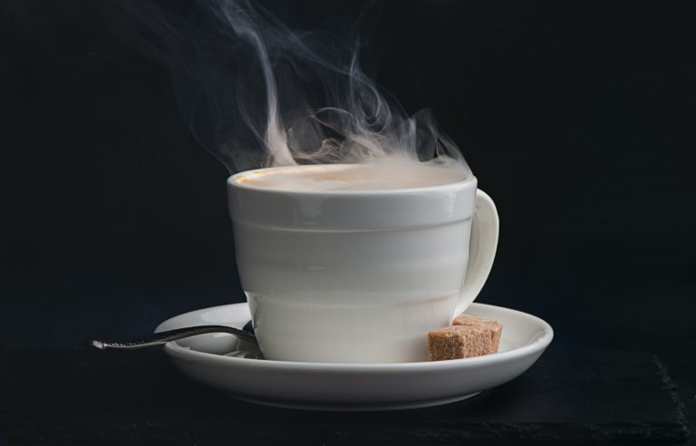 Steaming hot cup of coffee on a dark background with copy space